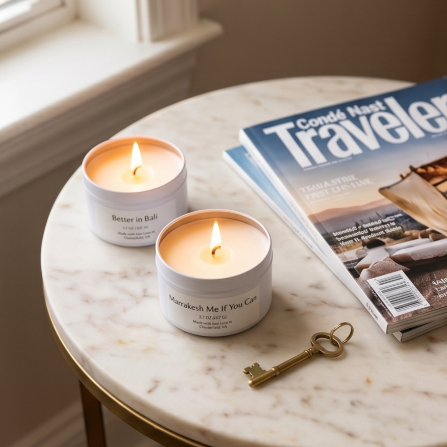 Two lit candles in white containers on a marble table with a 'Conde Nast Traveler' magazine and a key.