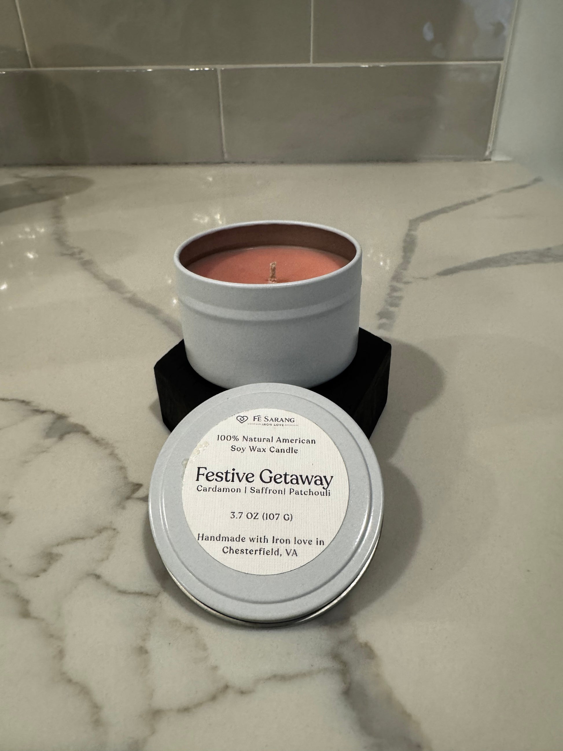 Candle in a metal container with a label on a marble surface