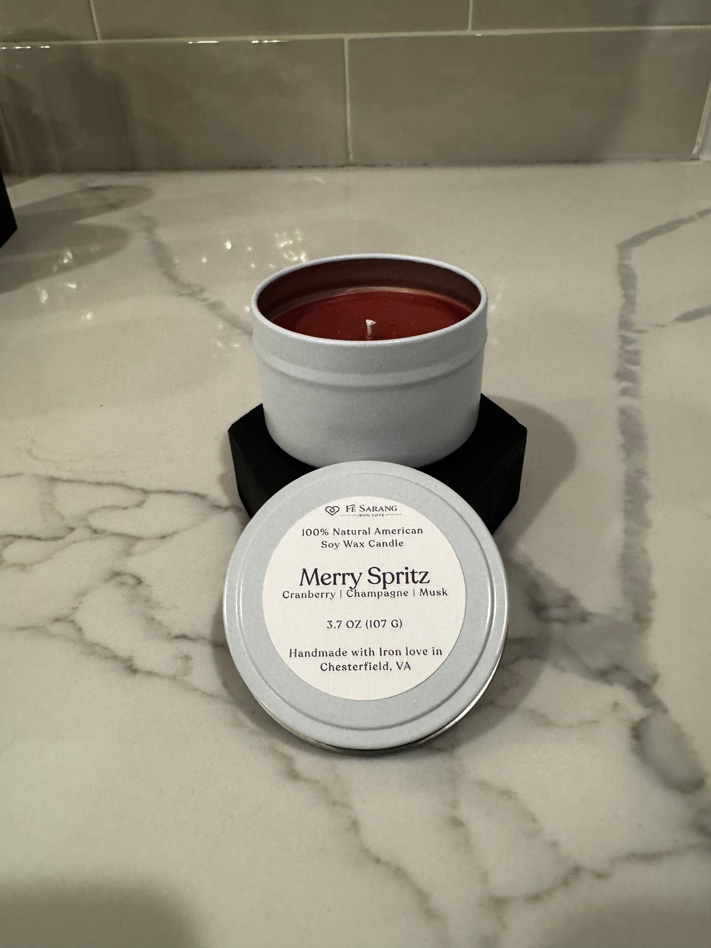 Candle in a tin with a label on a marble surface